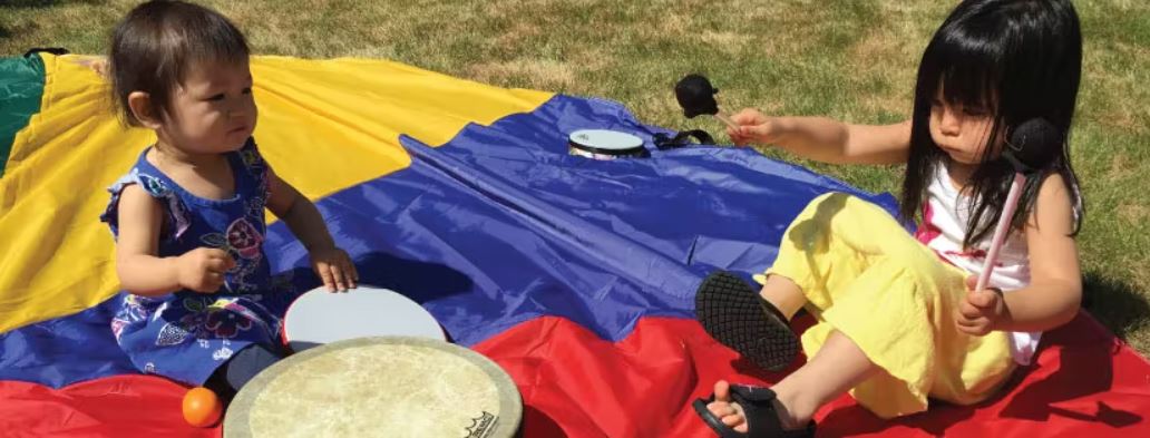 Young children playing with drums, sitting on a parachute.