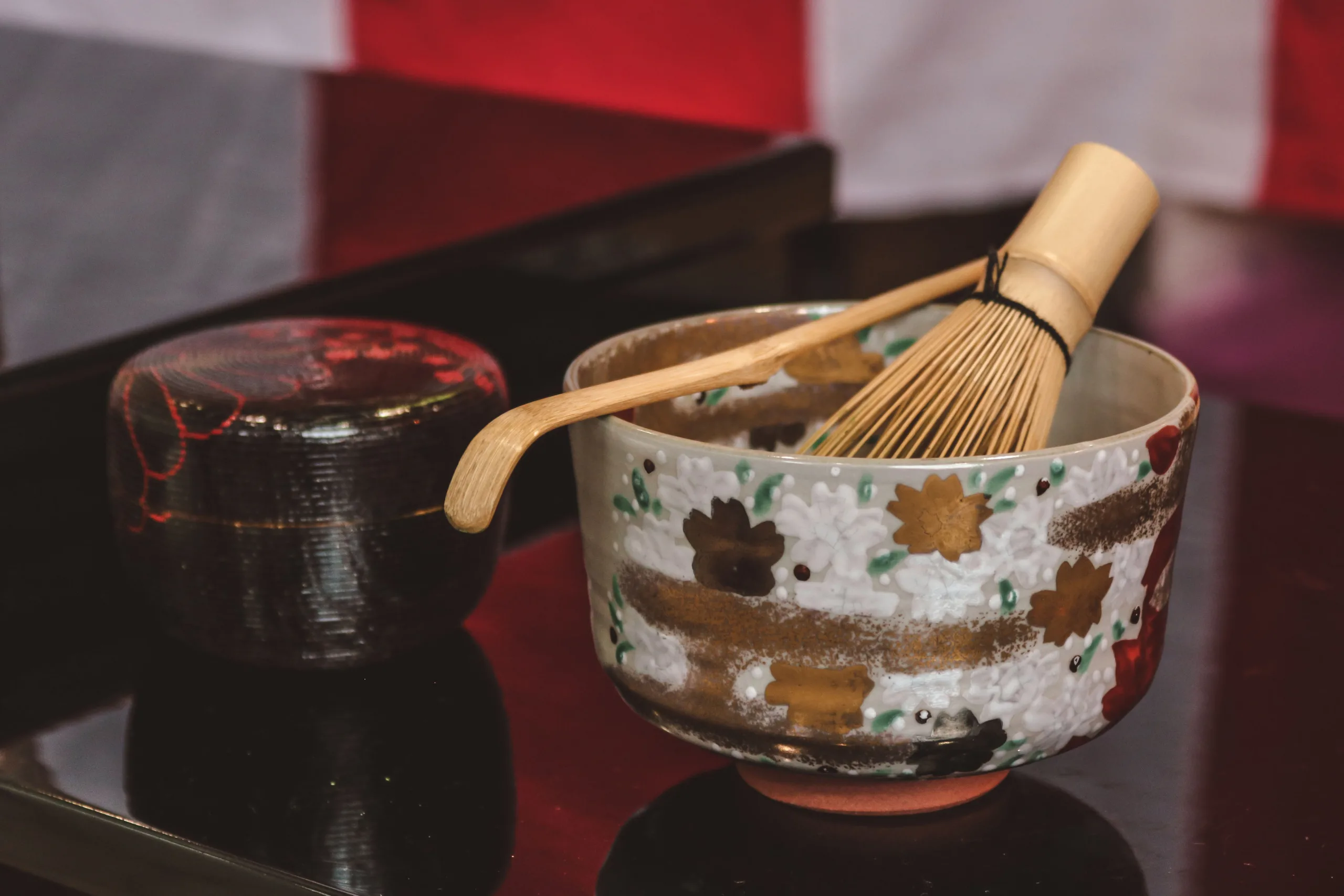 Japanese tea ceremony bowl with chashaku, saji and tea container on black table.