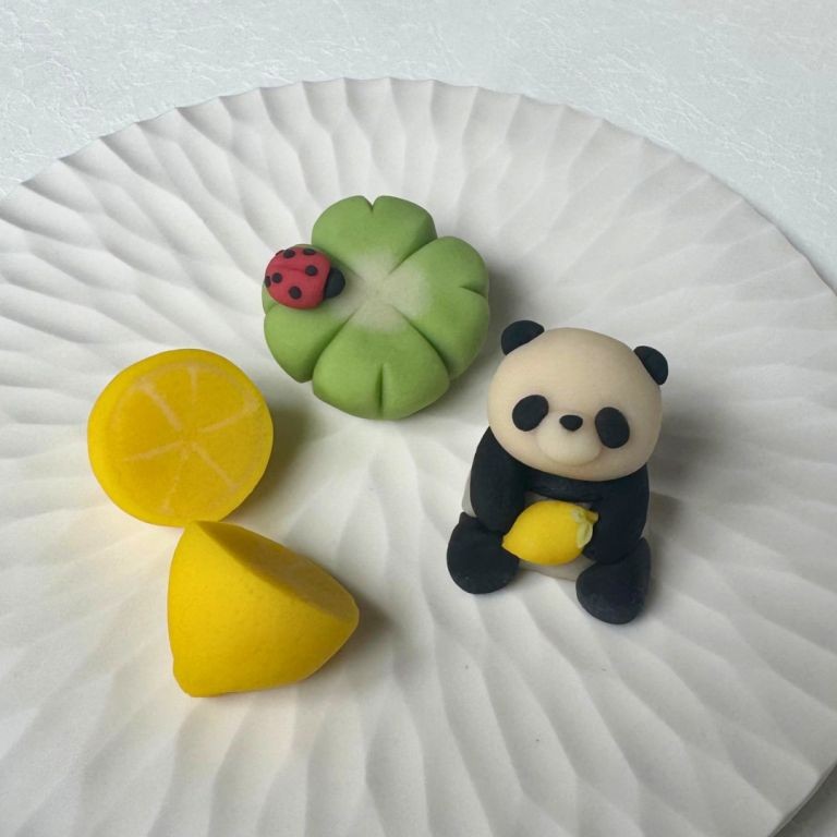 Nerikiri sweets on a white plate: a yellow lemon, a clover leaf with a ladybug, and a panda.
