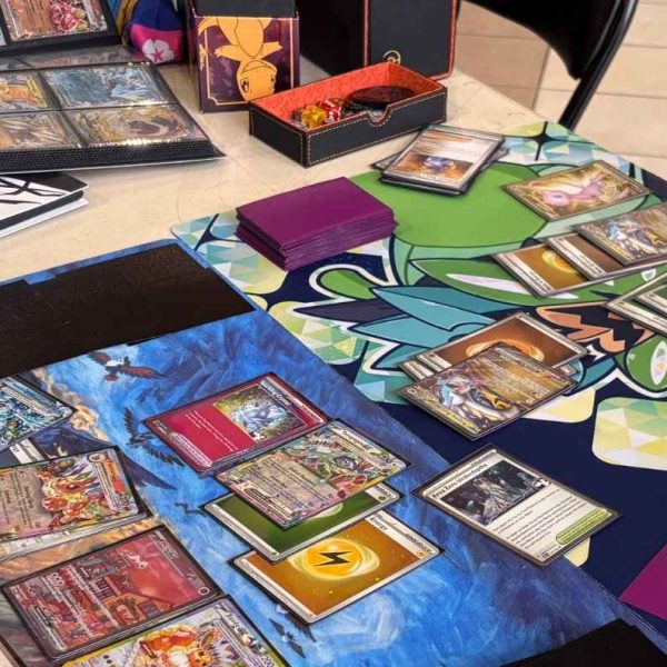 Two people playing the Pokémon Trading Card Game at a table, with cards arranged on colorful playmats.