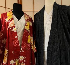 The image features a collage of four dress forms against a Japanese shoji screen. The leftmost mannequin shows a beige mesh compression undergarment designed to flatten the chest. The center mannequin displays white cotton under-layers padded with towels around the waist for shaping. Next to that is a red floral kimono. The rightmost mannequin shows a male-style ensemble featuring a white base layer under a dark pinstriped textured robe.