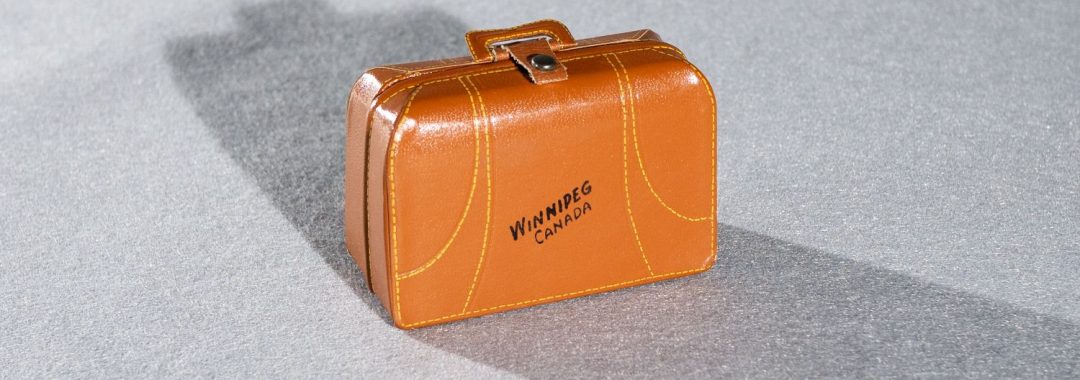 Tiny brown leather suitcase with Winnipeg, Canada in black letters photographed ethafoam with a long shadow.