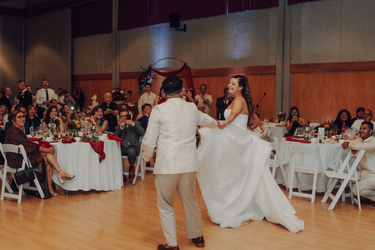A bride and groom dressed in white dancing in front of their guests at a wedding party.