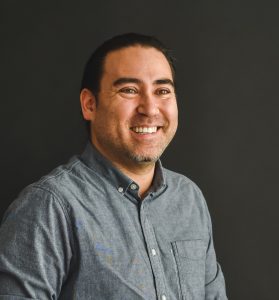 Headshot of Jeff Chiba Stearns smiling in a grey shirt.
