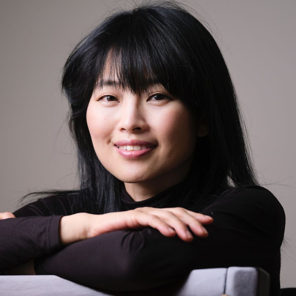 A Japanese lady dressed in black smiling with her arms crossed.